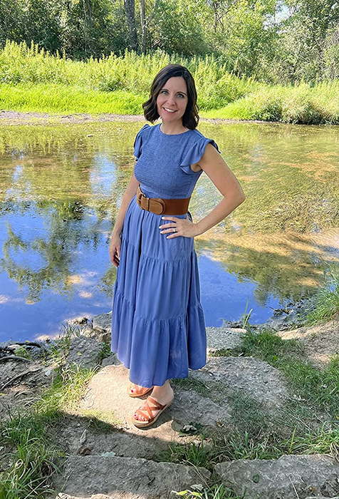 reviewer wearing the blue dress, posing by a pond