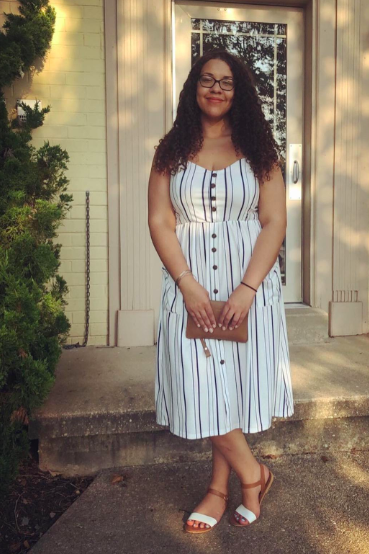 A reviewer wearing a white spaghetti strap dress with vertical stripes.