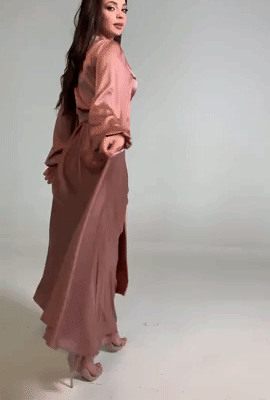 A model strides confidently in a long-sleeve, maxi rose gold dress.