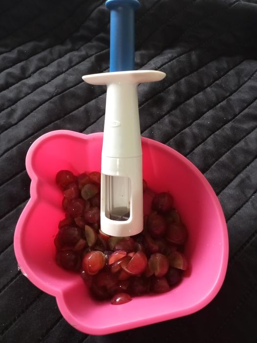 A grape cutter tool with halved grapes in a pink bowl, designed for quick and child-safe food prep