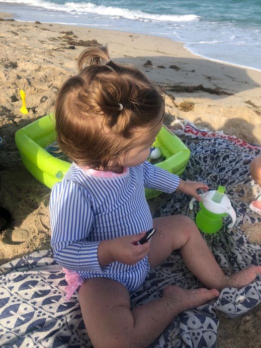 Toddler playing on the beach with toys, dressed in a RuffleButts swimsuit