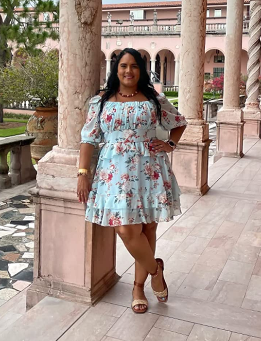 The reviewer is wearing the same dress in blue, accessorized with nude sandals, standing in front of brown pillars.