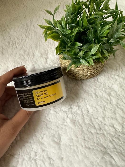 A reviewer is holding the jar of the Cosrx Snail Mucin cream.