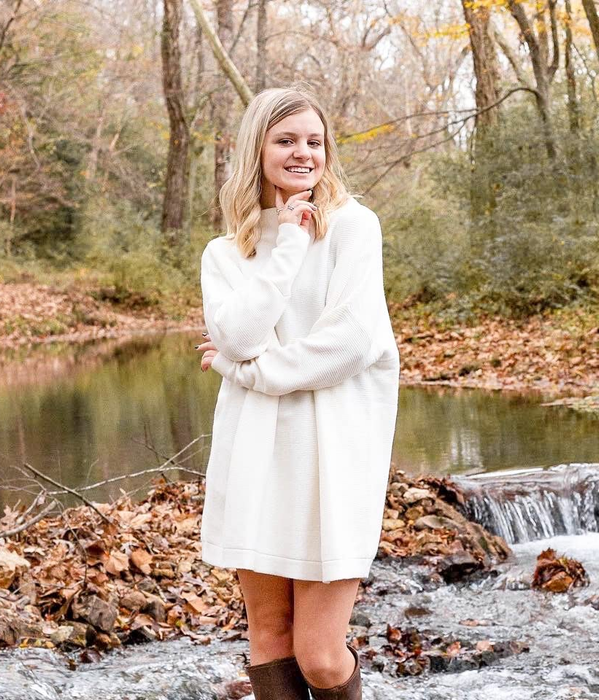 reviewer modeling the white sweater dress amidst fall leaves