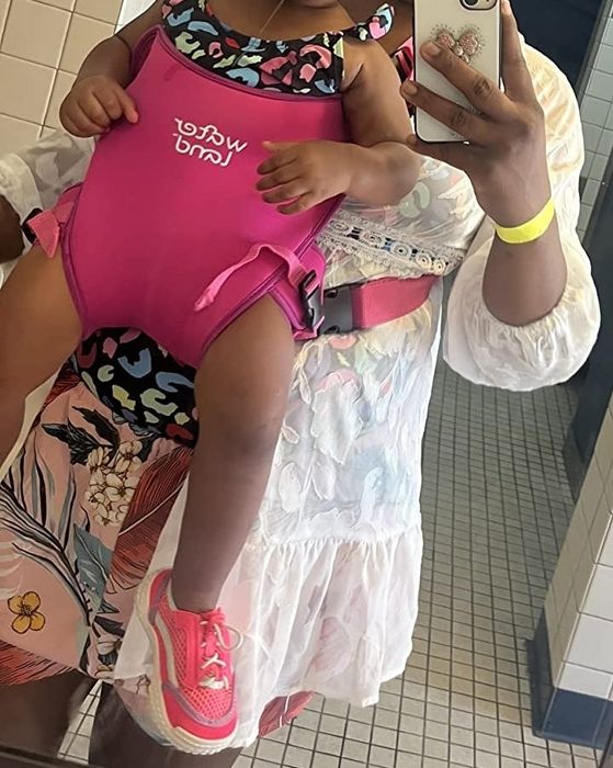 A woman poses in front of a mirror with her child comfortably secured in a carrier, ready for adventure.