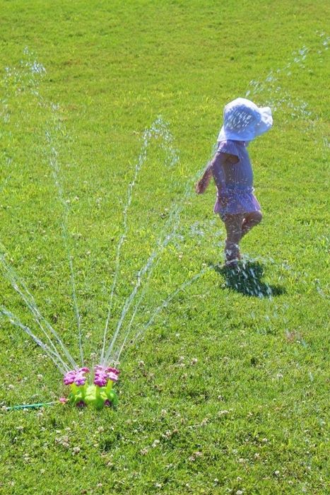 A child enjoys playing with a sprinkler on a sunny day in the garden, perfect for a summer-themed shopping article.