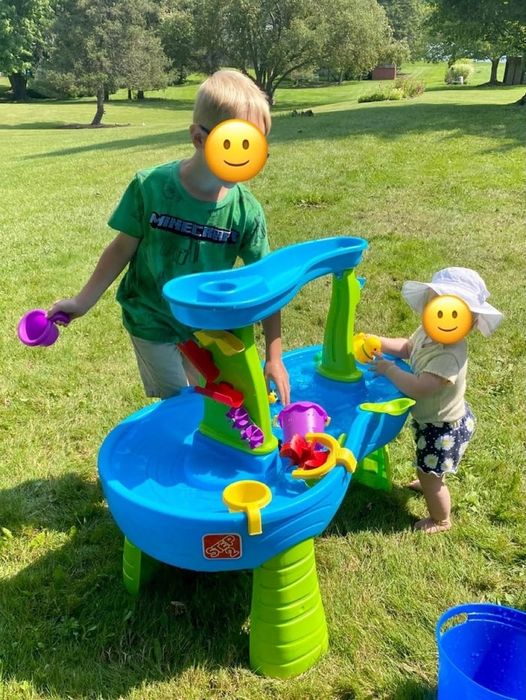 Two kids happily playing with a water table outdoors
