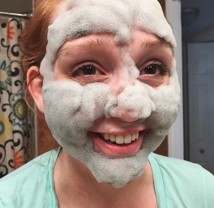 The reviewer happily wearing a foamy face mask, smiling.