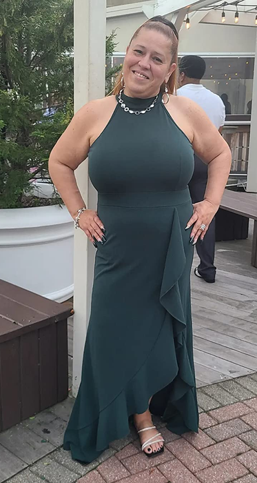 The reviewer is wearing a dark green halter maxi dress with a ruffled side slit and a matching bottom, accessorized with a necklace and strappy heels.