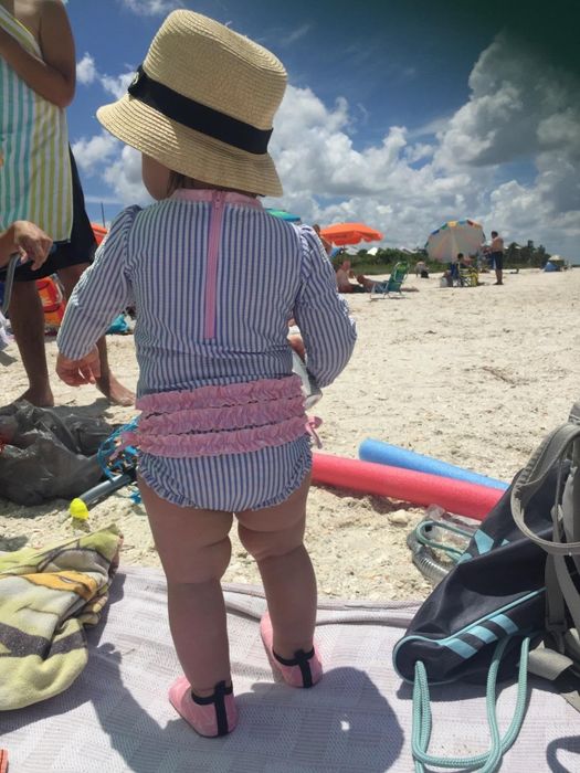 A baby at the beach in a RuffleButts swimsuit