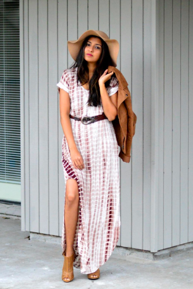 A reviewer wearing the brown and white dress with a belt and floppy hat, striking a pose with one leg through the high slit