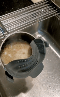 a gif showing a clip-on strainer being used to drain pasta