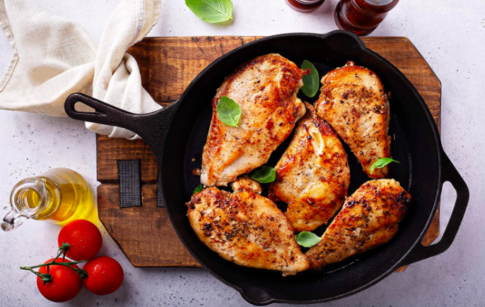 A black cast-iron skillet filled with grilled chicken breasts and garnished with fresh basil leaves
