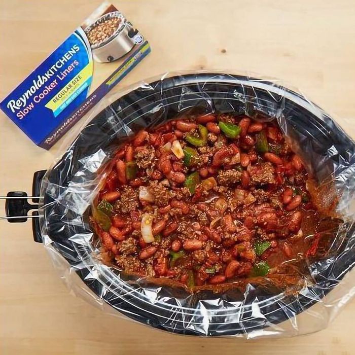 A slow cooker liner filled with hearty chili containing beans, meat, and vegetables, shown alongside its packaging