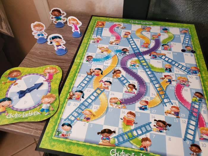 A Chutes and Ladders game setup with playful cartoon characters as pieces, accompanied by a spinner, all set on the table, ready for the action to begin.