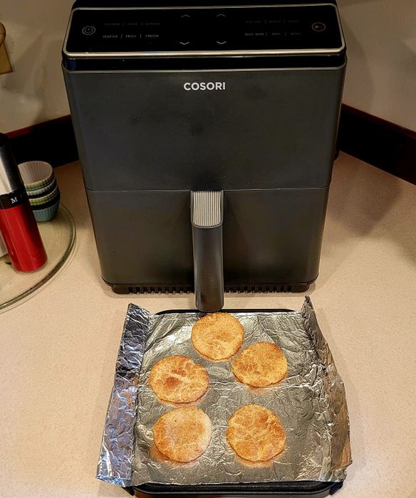 An air fryer on a countertop with four freshly baked cookies on foil, showcasing its versatility for healthier cooking