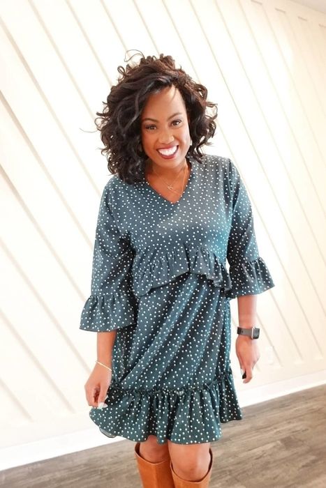 A reviewer wearing a teal three-quarter sleeve dress with white polka dots, paired with brown tall boots.