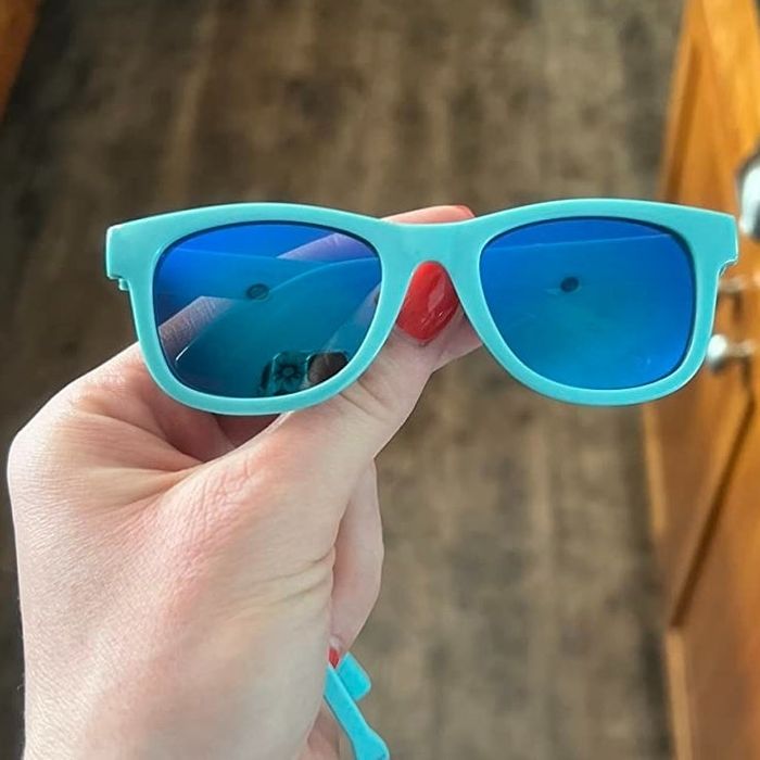 A hand holds blue-lensed sunglasses against a kitchen backdrop, perfect for accessory shopping.