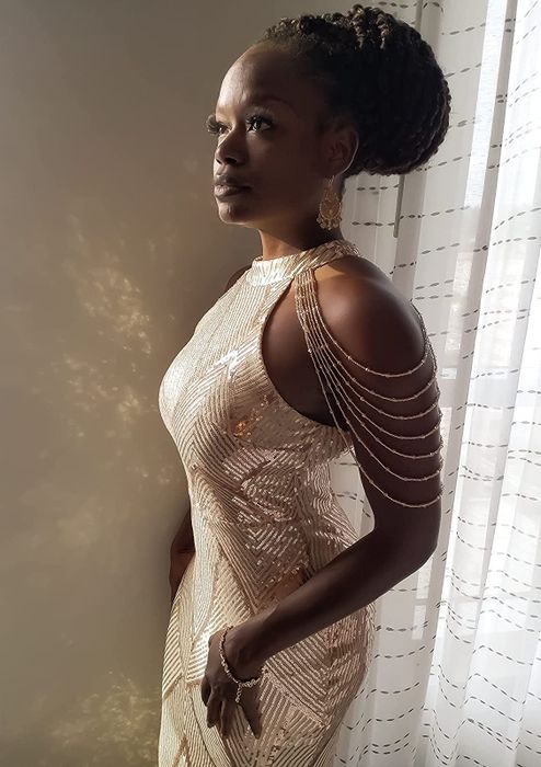 A reviewer wearing the white version of the dress, standing in front of a sheer white curtain