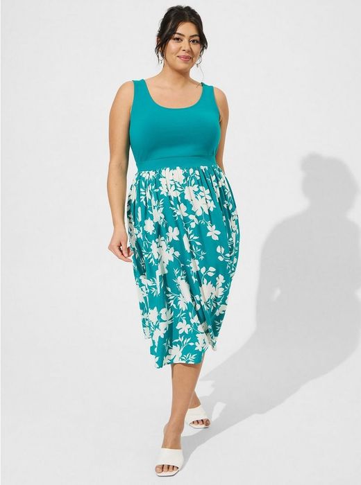A model in a teal midi dress featuring a scoop neck, sleeveless design, solid bodice, and a skirt adorned with white flowers.