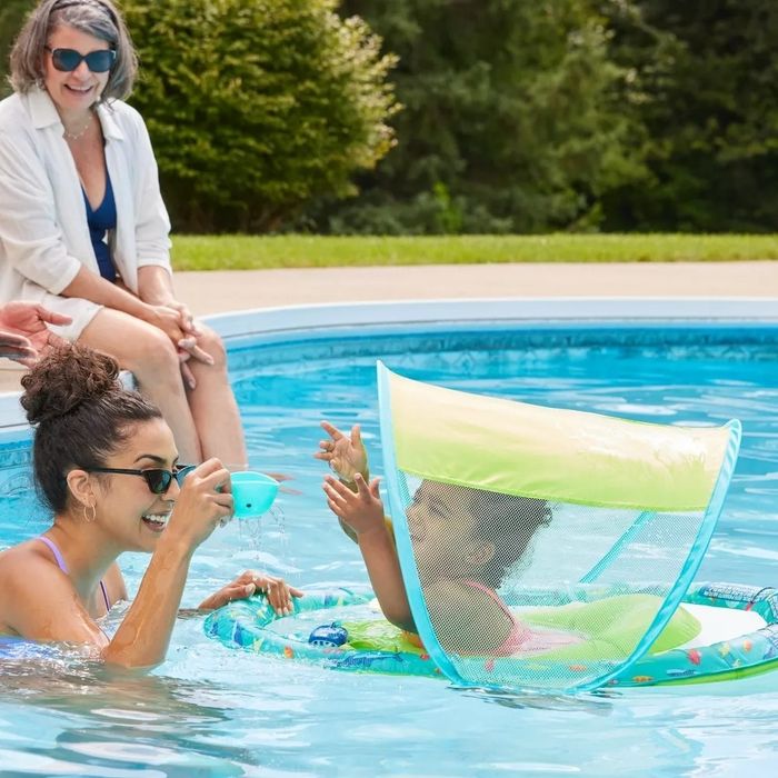 A woman and child relax together in a pool, sheltered by a floating sunshade.