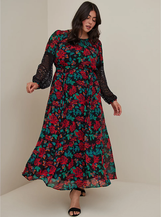 The model is wearing a maxi dress with a crew neckline featuring a red floral pattern and black lace long sleeves, paired with black open-toe heels against a white backdrop.