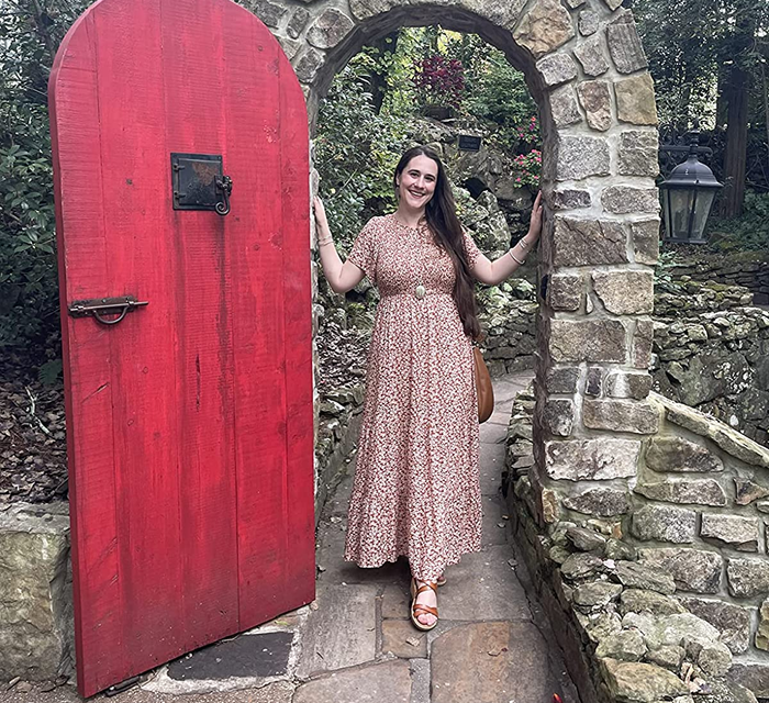 reviewer posing in the red and white floral dress under an archway
