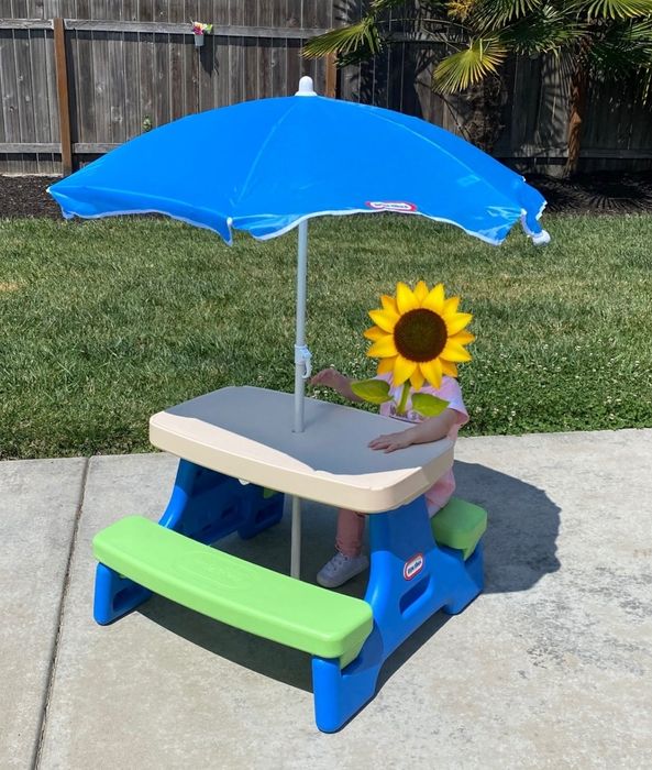 A child sitting comfortably at a picnic table, shaded by an umbrella for a pleasant outdoor experience.