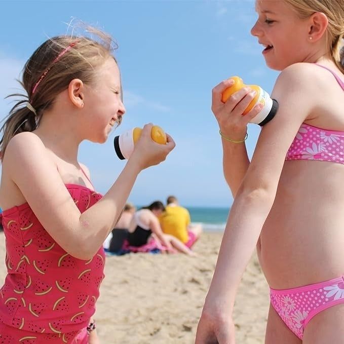 Two children enjoying the beach while applying sunscreen with their Solar Buddies applicators.