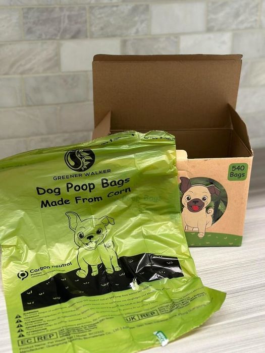 Eco-friendly dog poop bags in packaging featuring a cartoon dog, with details highlighting their corn-based and carbon-neutral properties. Box contains 540 bags