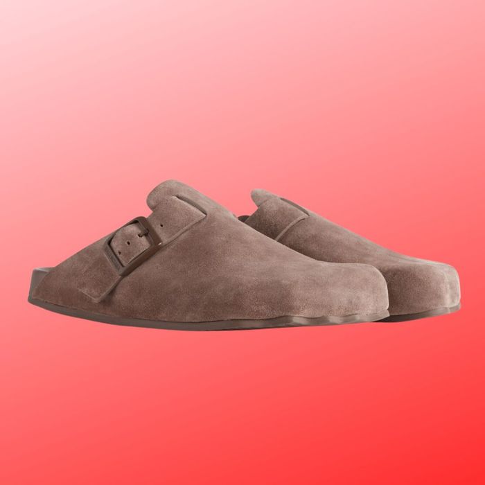 A pair of brown suede clogs featuring a buckle, set against a red gradient backdrop