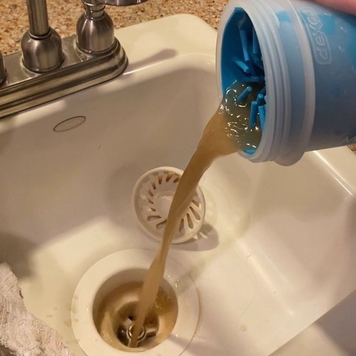 A reviewer pouring out the dirty, muddy water from the paw cleaning device.