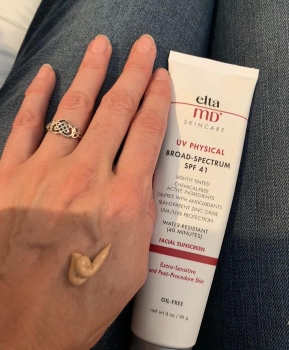 A reviewer's hand with a tan-colored sunscreen applied.