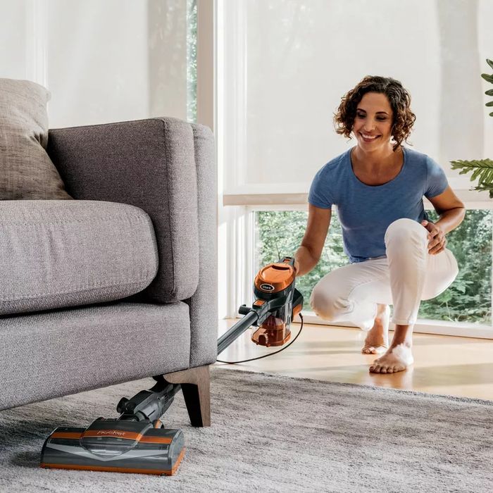 A person using a handheld Shark vacuum under the couch, showing how easy it is to maneuver in a home environment