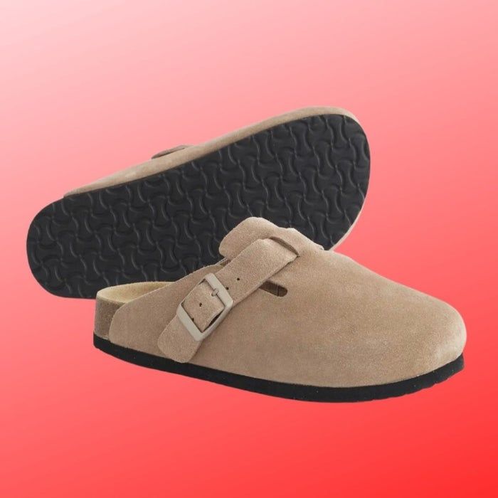 Tan suede slip-on clogs with a buckle, resting on thick black soles, showcased against a gradient backdrop
