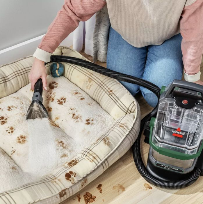 Person uses a portable carpet cleaner to clean a dog bed covered in muddy paw prints