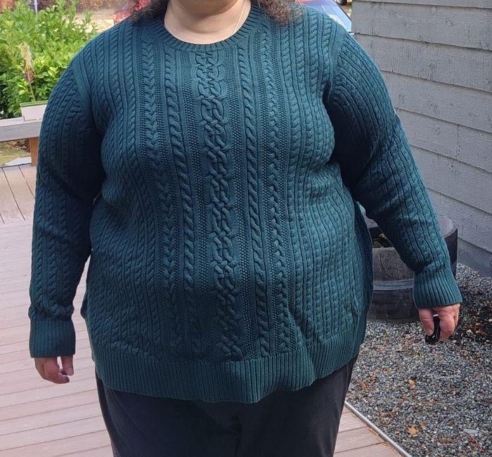 plus-size reviewer modeling a green cable knit sweater