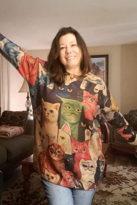 A reviewer smiling while wearing a cozy sweater featuring a colorful cat design, set in a relaxed living room