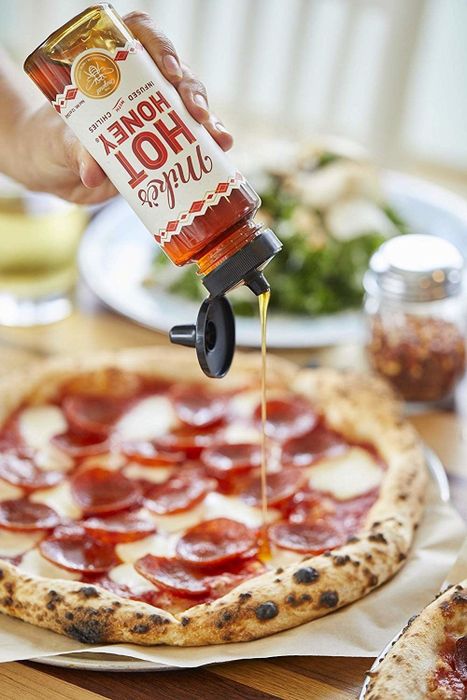 A bottle of honey drizzled over a slice of pizza