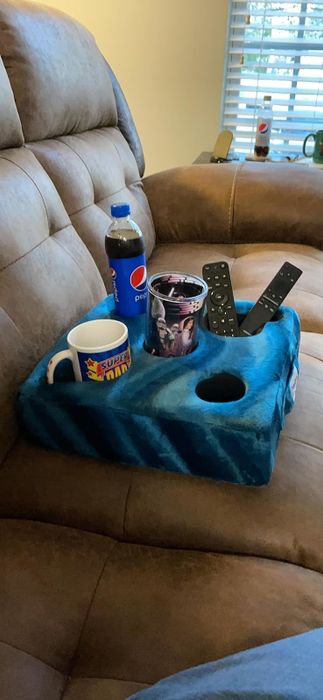 A blue pillow with five slots holding a can, a drink, a remote, and a phone