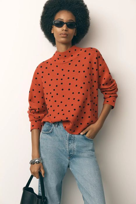 Person in a polka dot sweater and jeans, holding a bag and wearing sunglasses