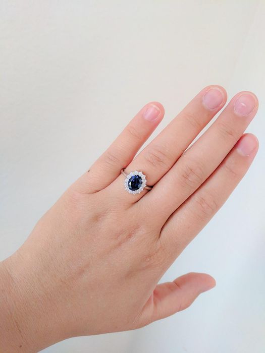 a reviewer showcasing the ring with a slim band, a central sapphire stone encircled by sparkling clear gems