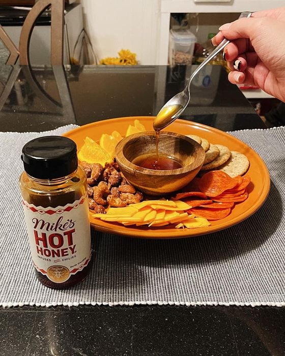 a reviewer drizzling Mike's Hot Honey over nuts and cured meats