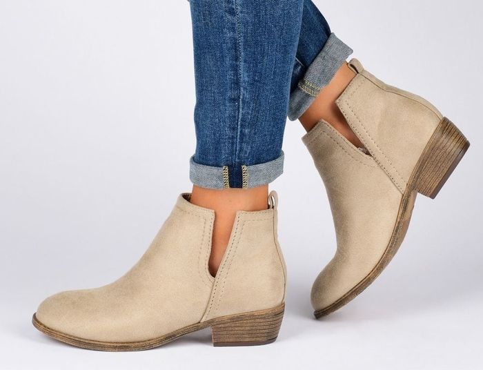 A close-up shot of an individual wearing beige suede ankle boots paired with jeans, highlighting a chic yet relaxed footwear choice.