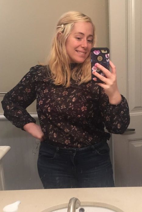 Person capturing a mirror selfie in a patterned blouse and jeans, smiling