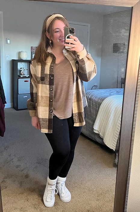 Reviewer in a tan plaid shacket, paired with a beige top, black leggings, and white sneakers, capturing a mirror selfie in a bedroom