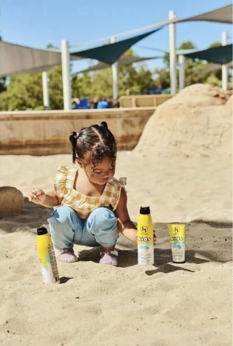 A child at a playground with three bottles of sunscreen, highlighting the importance of sun safety during outdoor play