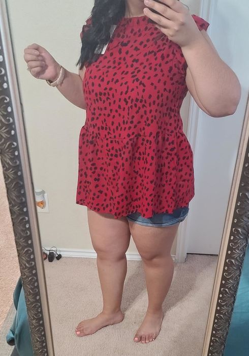 Individual in a red leopard-print top and denim shorts snaps an indoor mirror selfie