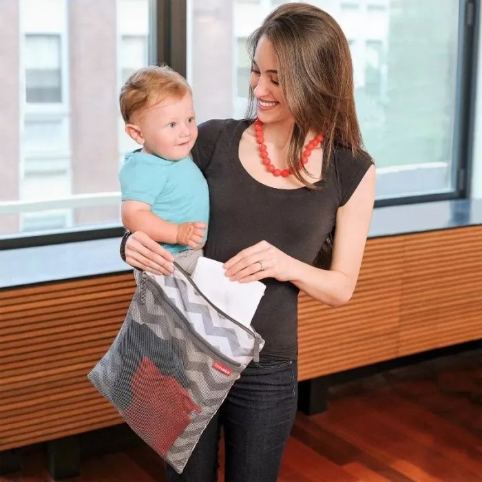 A mother holding a child while carrying a stylish diaper bag, smiling warmly, highlighting a practical yet fashionable accessory for parents