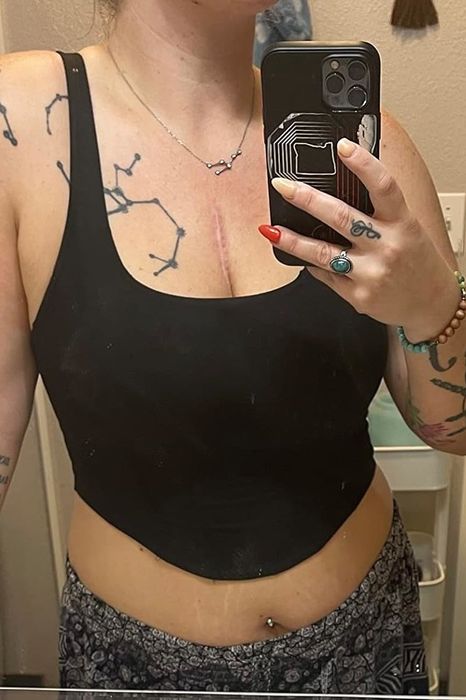 Person capturing a mirror selfie, wearing a black crop top with visible arm tattoos